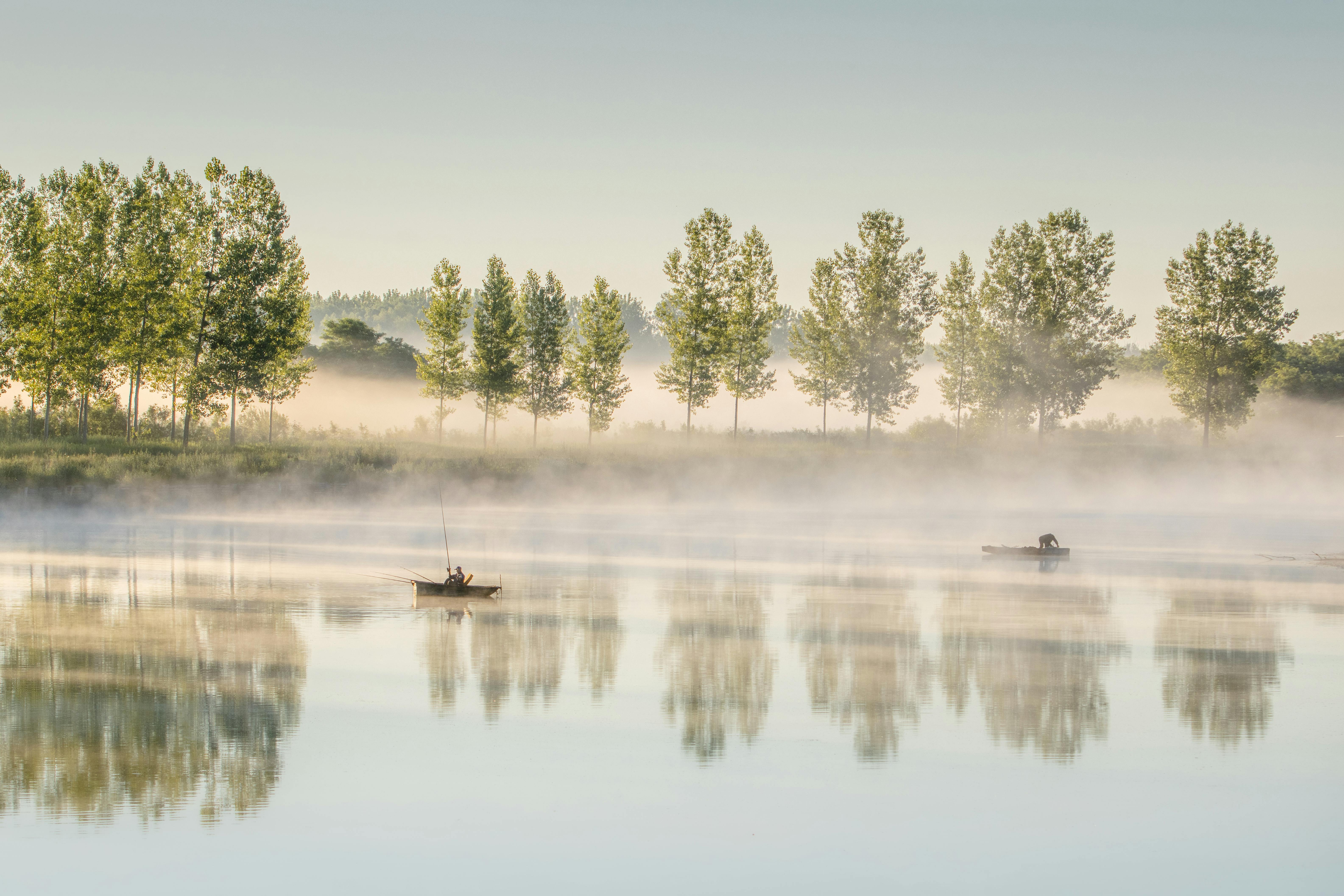 Fishermen on a misty lake at dawn in Bilje, Croatia, surrounded by reflections and serene nature.
