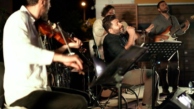 Group of musicians performing on stage at night with various instruments.