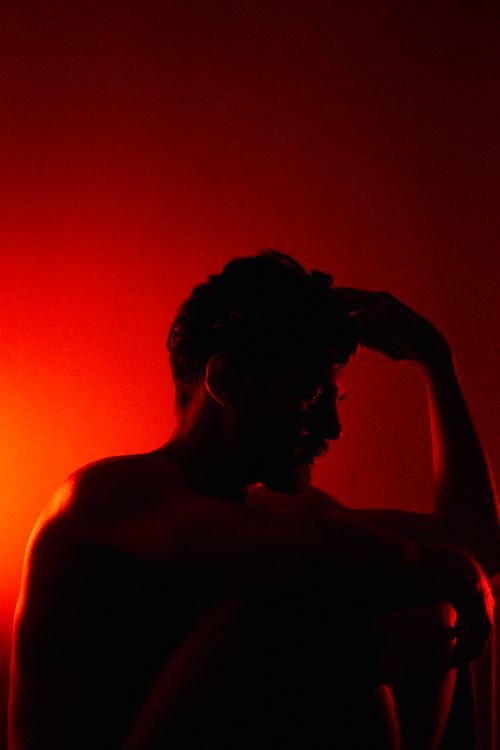 Free A silhouette of an adult man, deep in thought, set against a dramatic red background. Stock Photo
