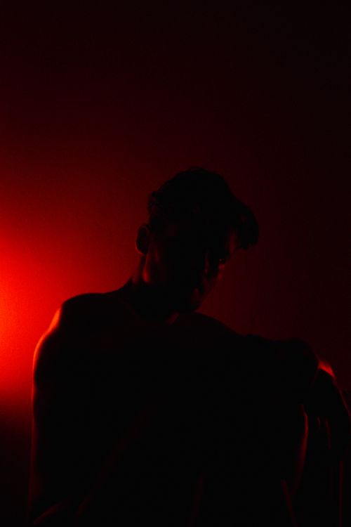 Free Silhouette of a man against a dark background illuminated by red light for dramatic effect. Stock Photo