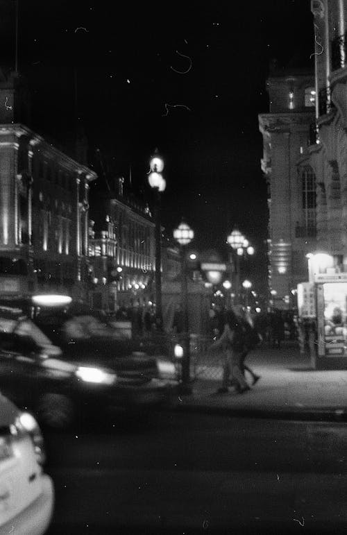 A Grayscale Photo of People Walking on the Street Near Buildings at Night