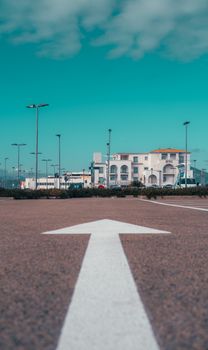 Low-angle view of an arrow on asphalt pointing towards urban buildings under blue sky.