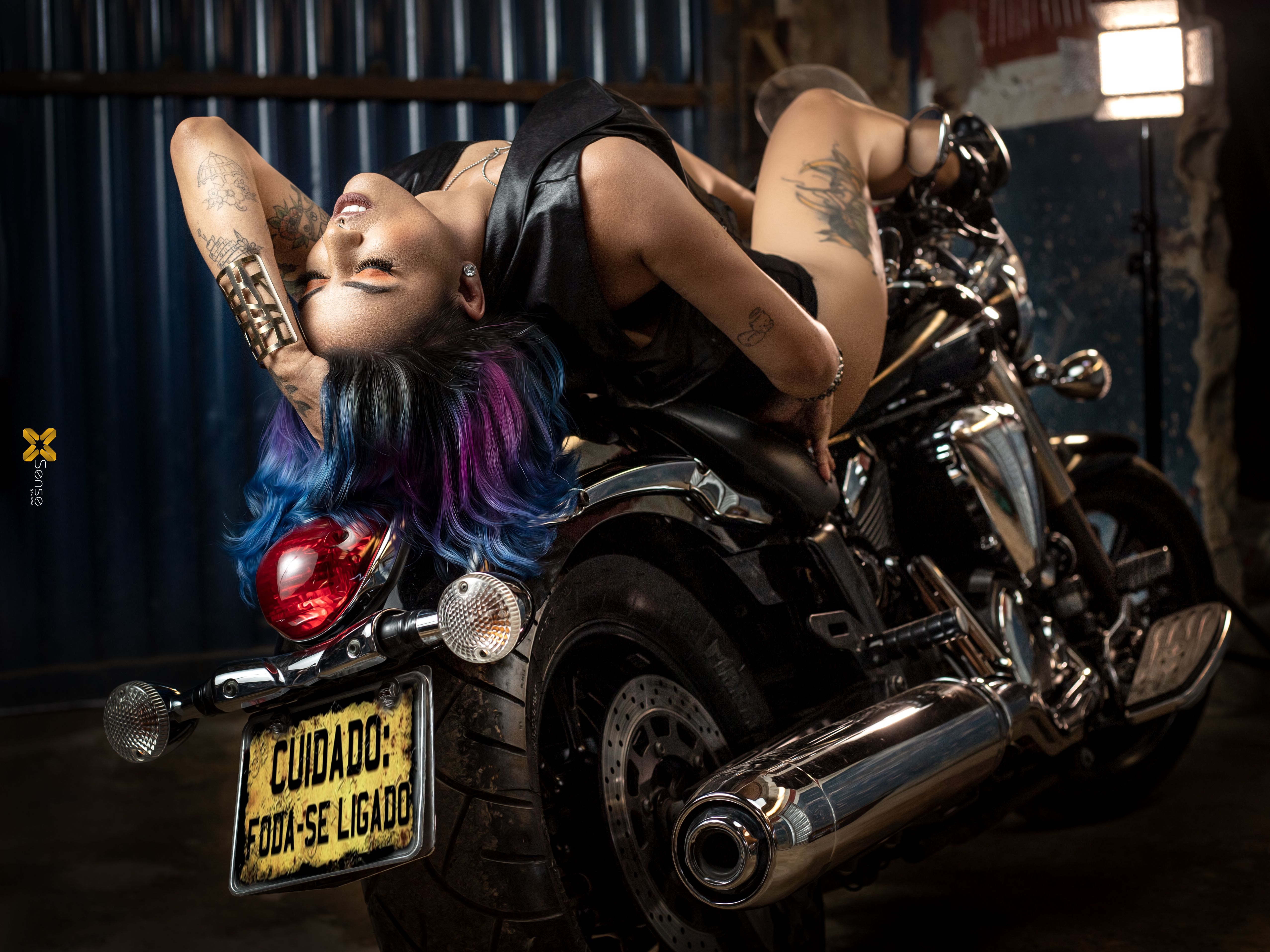Dynamic woman with vibrant hair posing on motorcycle in urban setting.