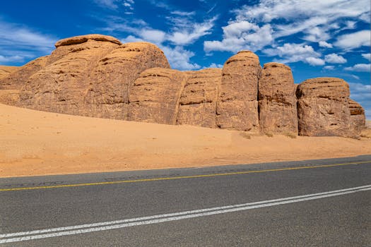 Experience the beauty of arid landscapes with striking rock formations along a quiet road under a bright blue sky.