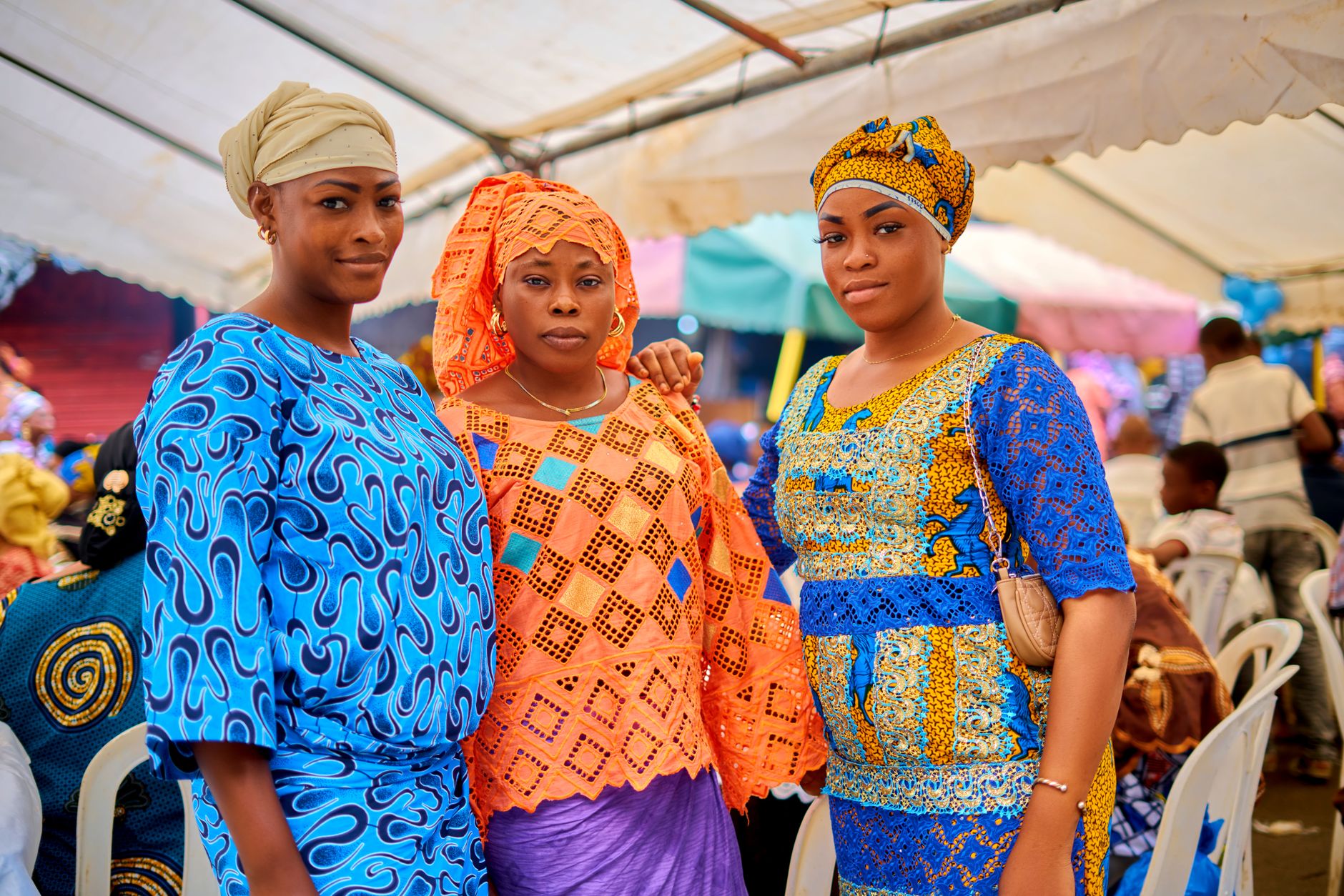 Three women in traditional African clothing at a lively cultural event in Abidjan.