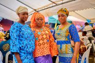 Three women in traditional African clothing at a lively cultural event in Abidjan.
