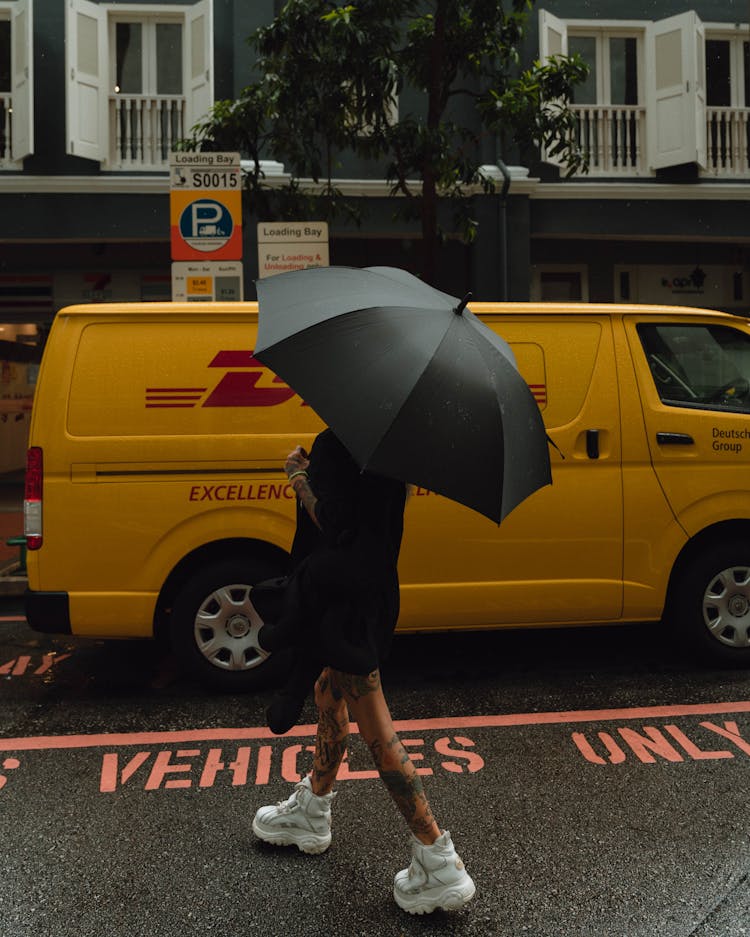 Woman With Umbrella And Tattoos Walking By A Post Delivery Van