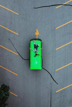 Drone shot of a person lying on a green truck in an empty parking lot.