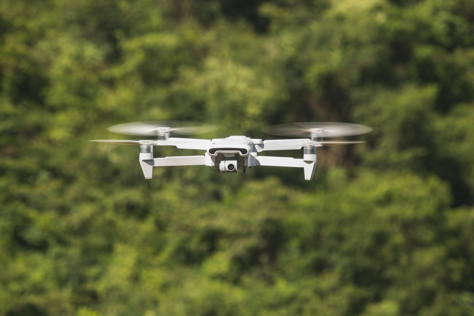 A modern drone in flight against a vibrant green forest backdrop, showcasing drone technology.