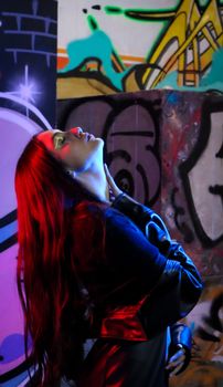 A stylish woman in a black leather jacket poses against a vibrant graffiti wall in an urban setting.