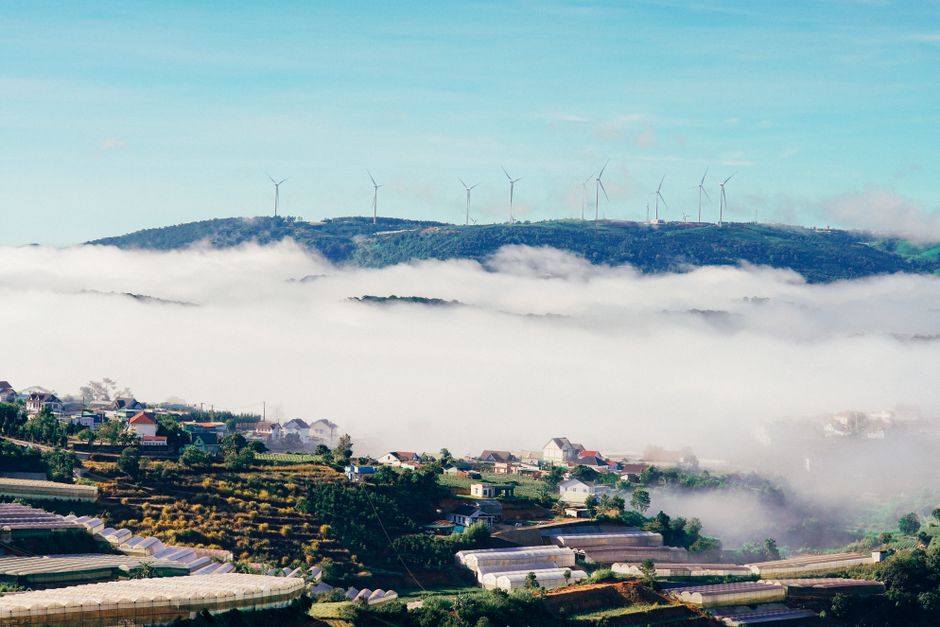 A stunning aerial view of Dalat's misty landscape with wind turbines and houses under a cloud-filled sky.