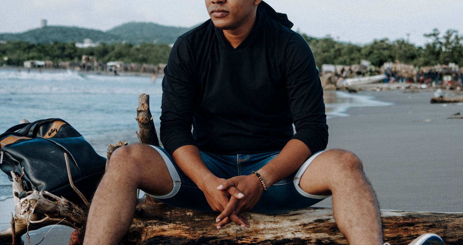 Man in Black Crew Neck T-shirt Sitting on White and Blue Surfboard on Beach during in Pereira, Colombia.