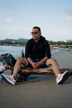 Man in black hoodie relaxing on a beach in Puerto Colombia, showcasing a laid-back summer vibe.
