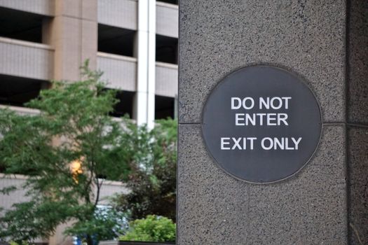 A 'Do Not Enter' sign on a concrete wall outside a building with greenery.