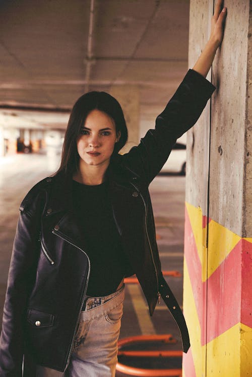 A Woman in Black Leather Jacket Standing Near the Concrete Wall
