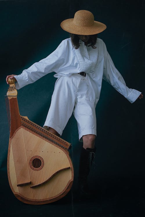 A Woman in White Long Sleeves and Shorts Holding a Bandura while Wearing a Hat