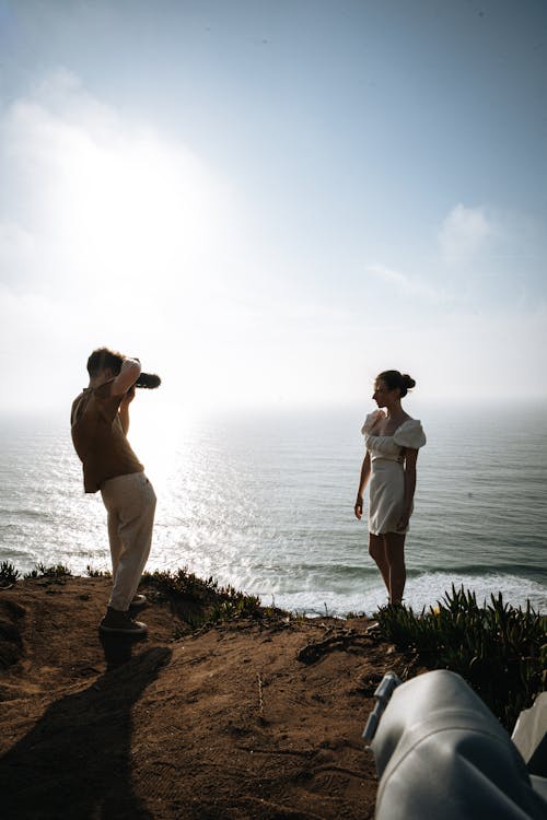 Man Taking Photo of Woman on Cliff by the Sea