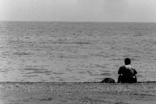 A person sits alone on the beach in Málaga, Spain, gazing at the sea.