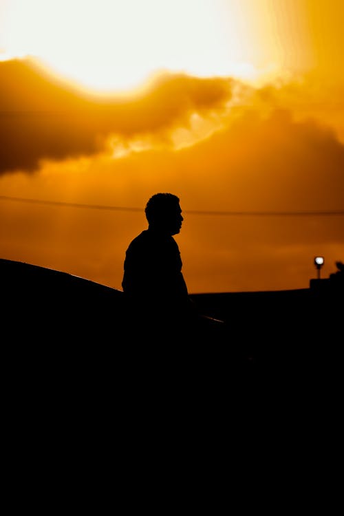 Foto profissional grátis de cair da noite, céu alaranjado, homem