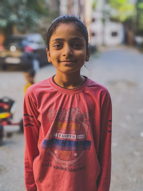 Free A cheerful Indian girl stands outdoors, wearing a pink long sleeve shirt, smiles warmly. Stock Photo
