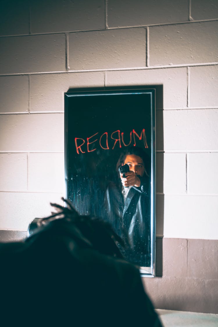 Photo Of A Man Reflecting In A Mirror And Keeping Up A Gun In His Hand