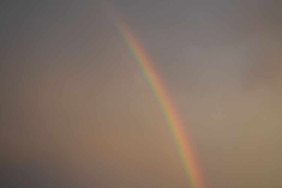 A stunning rainbow arches gracefully across a tranquil sky, creating a vivid, natural spectacle.