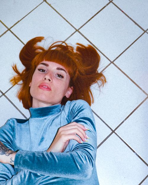 Free A woman with red hair and blue top lying on a white tiled floor, portrait style. Stock Photo