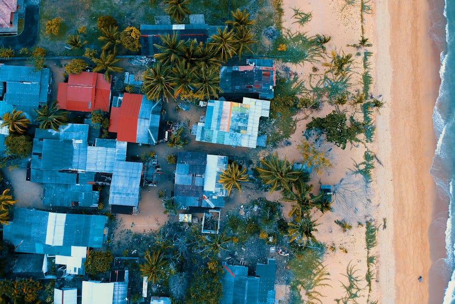 A stunning aerial shot of a beachside village with colorful roofs and ocean waves meeting sandy shores.