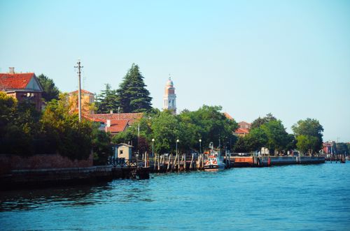 Free Scenic view of a Venetian canal with church in background and vibrant greenery lining the urban waterfront. Stock Photo