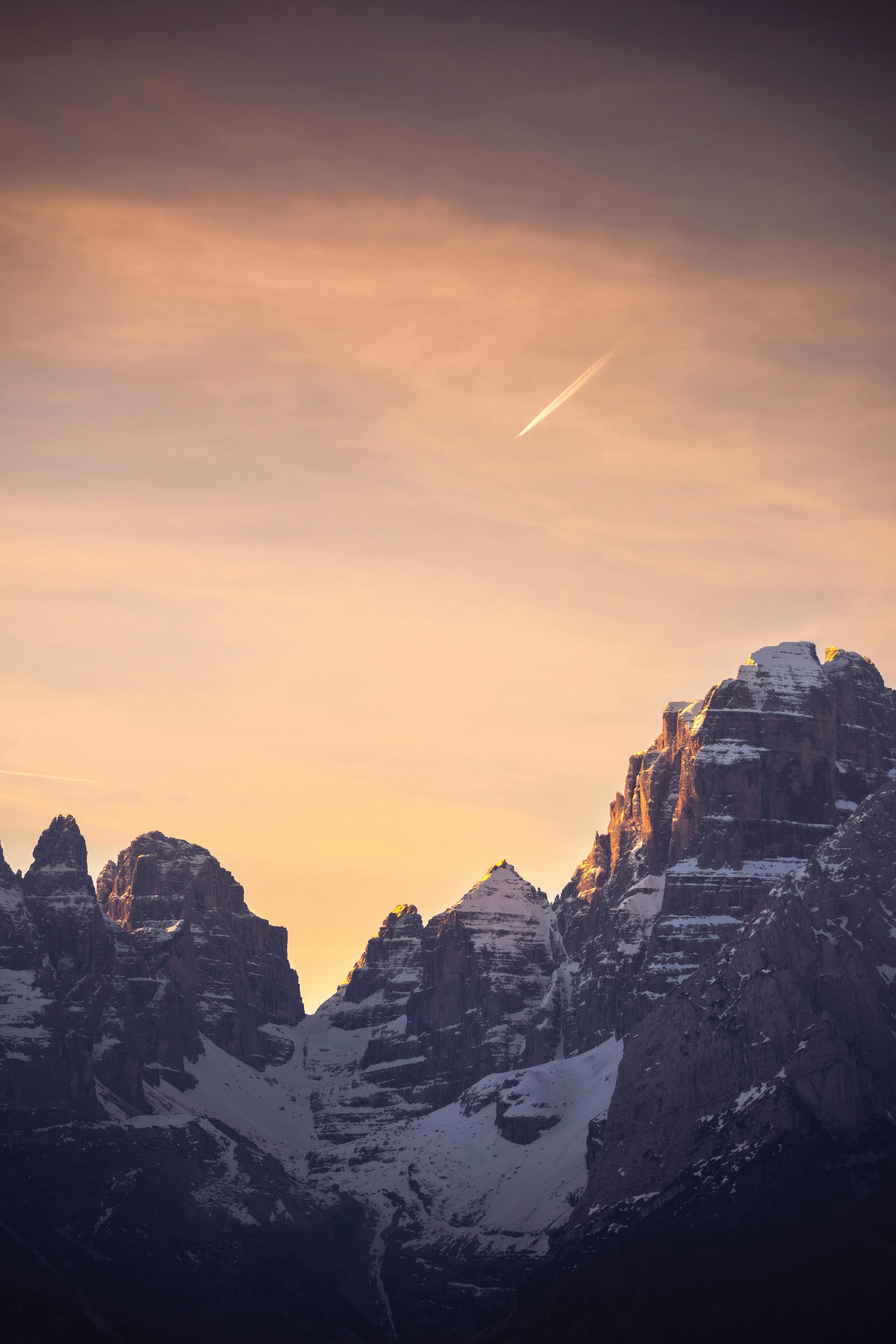 Golden sunset casting over snow-capped Dolomites in Italy with a visible comet in the sky.