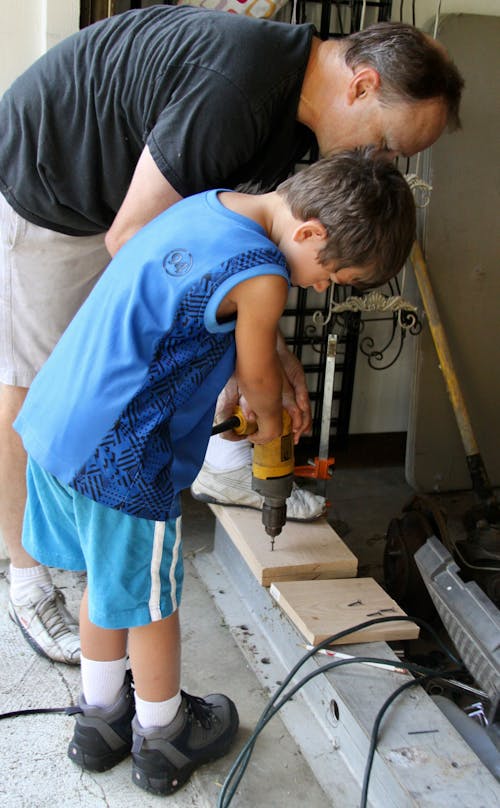 A Man and a Young Boy Drilling a Wood