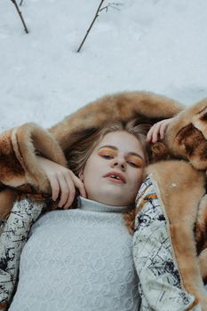 Elegant woman in fur coat lying on snow, showcasing winter fashion with modern artistic flair.