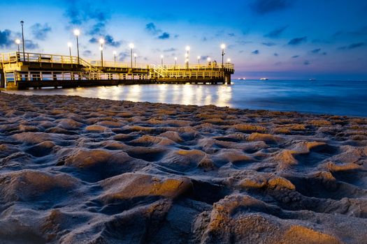 A serene evening view of the illuminated pier on the sandy beach in Gdańsk, Poland.