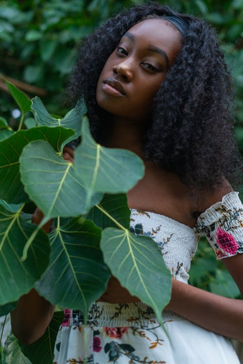 A Woman in White Off Shoulder Top Holding Green Leaves