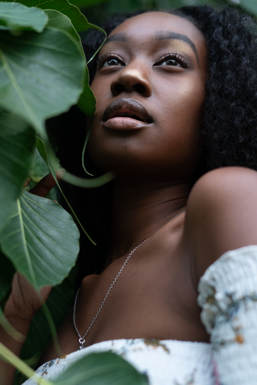 Free Close-up of a woman with curly hair surrounded by lush green leaves. Stock Photo