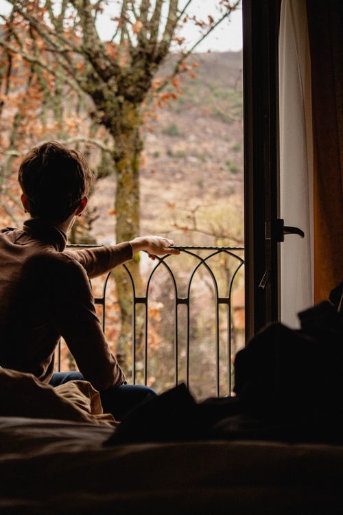 Free A woman looks out a hotel room window at a peaceful autumn landscape. Stock Photo