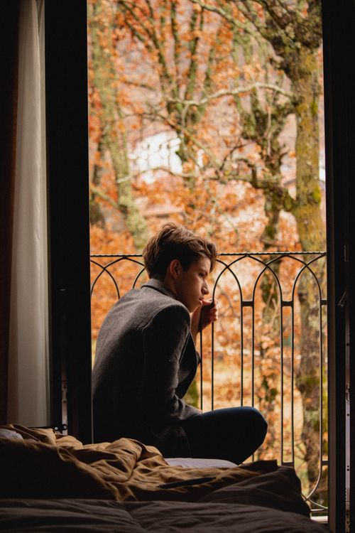 Free A thoughtful adult man sits on a balcony overlooking a fall landscape. Stock Photo