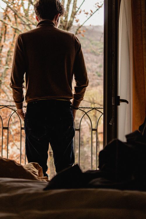 Free A man stands by a balcony overlooking an autumn landscape through a glass door. Stock Photo