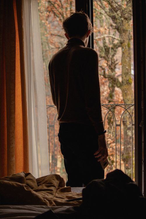 Free Man standing by window, holding phone, looking at autumn scenery. Stock Photo