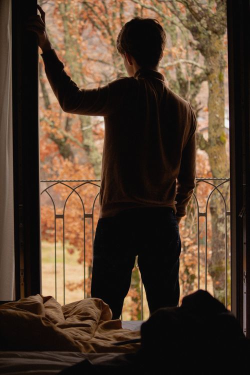 Free A man stands by a balcony door, enjoying the autumn view. Stock Photo