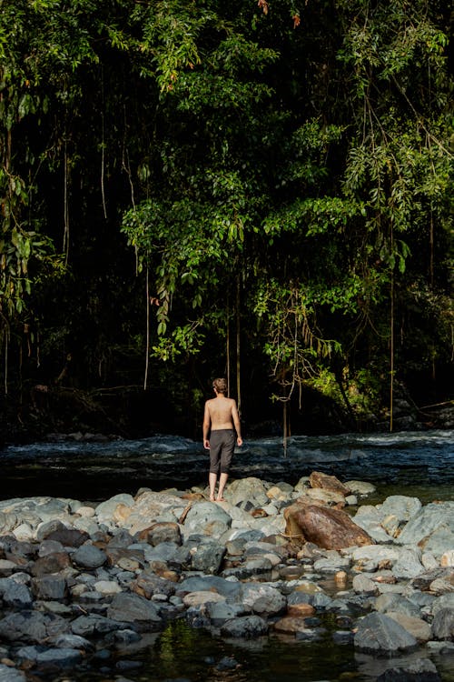 Shirtless Man Standing on Rock Beside the River