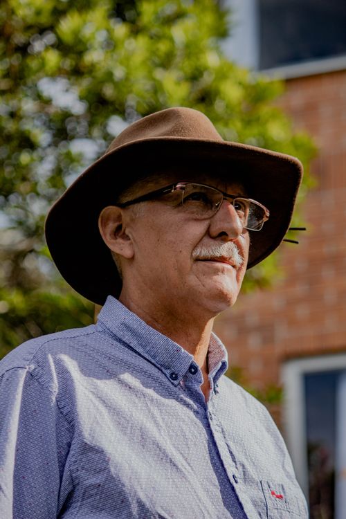 Free Senior man in glasses wearing a hat outdoors, looking thoughtful near a building. Stock Photo