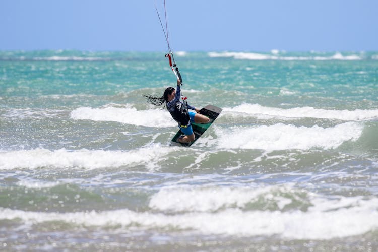 Person In Blue And Black Wetsuit Riding On Wakeboard On Sea Waves