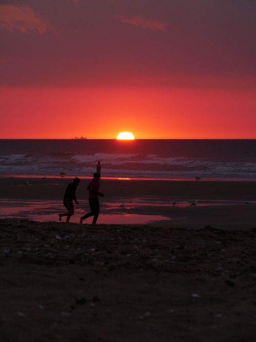 Free A vibrant sunset over Ouistreham Beach in France with silhouetted figures, capturing a serene moment. Stock Photo