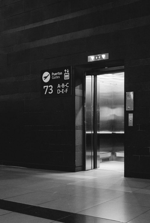 Free Black and white photo of an open elevator near Gate 73 in a modern building. Stock Photo