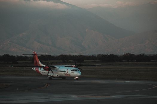A commercial plane on a runway with majestic mountains in the background, captured during twilight.