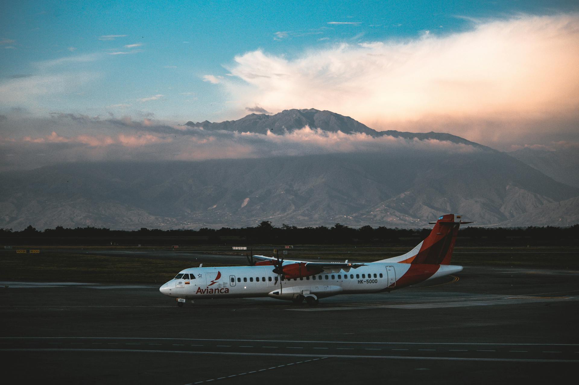 Avianca aircraft parked on tarmac with majestic mountains in the backdrop under a dramatic sky.