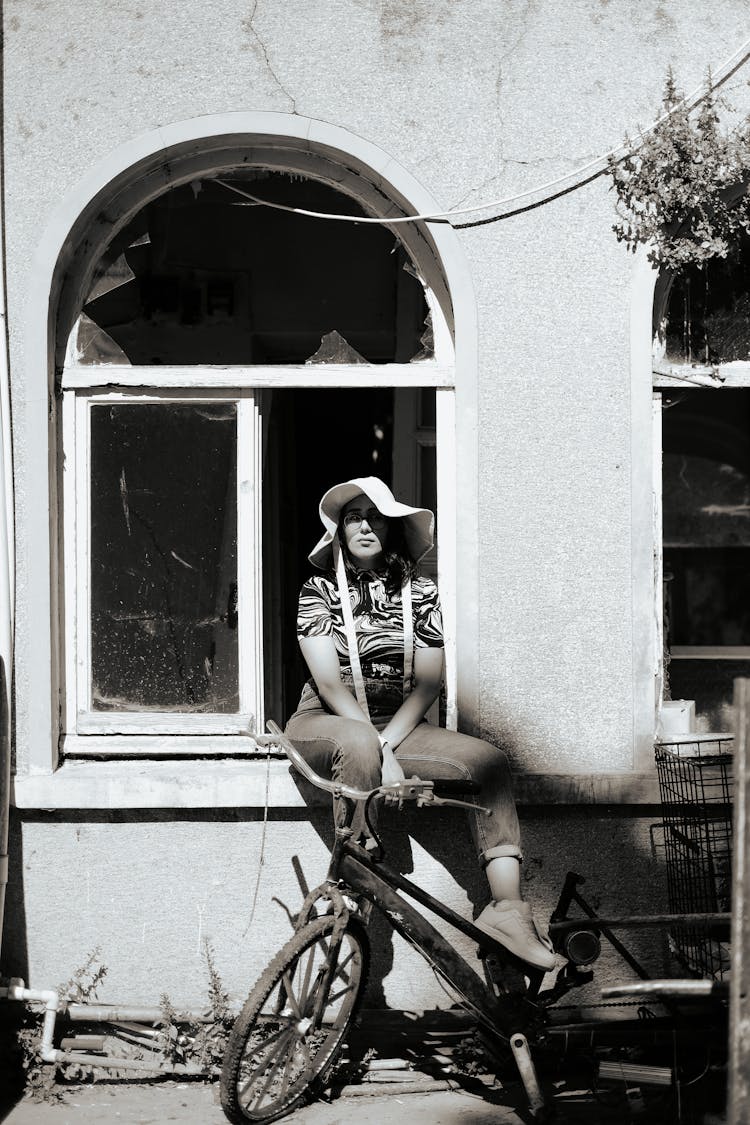 Woman With Bike Sitting At Window Near Old Building