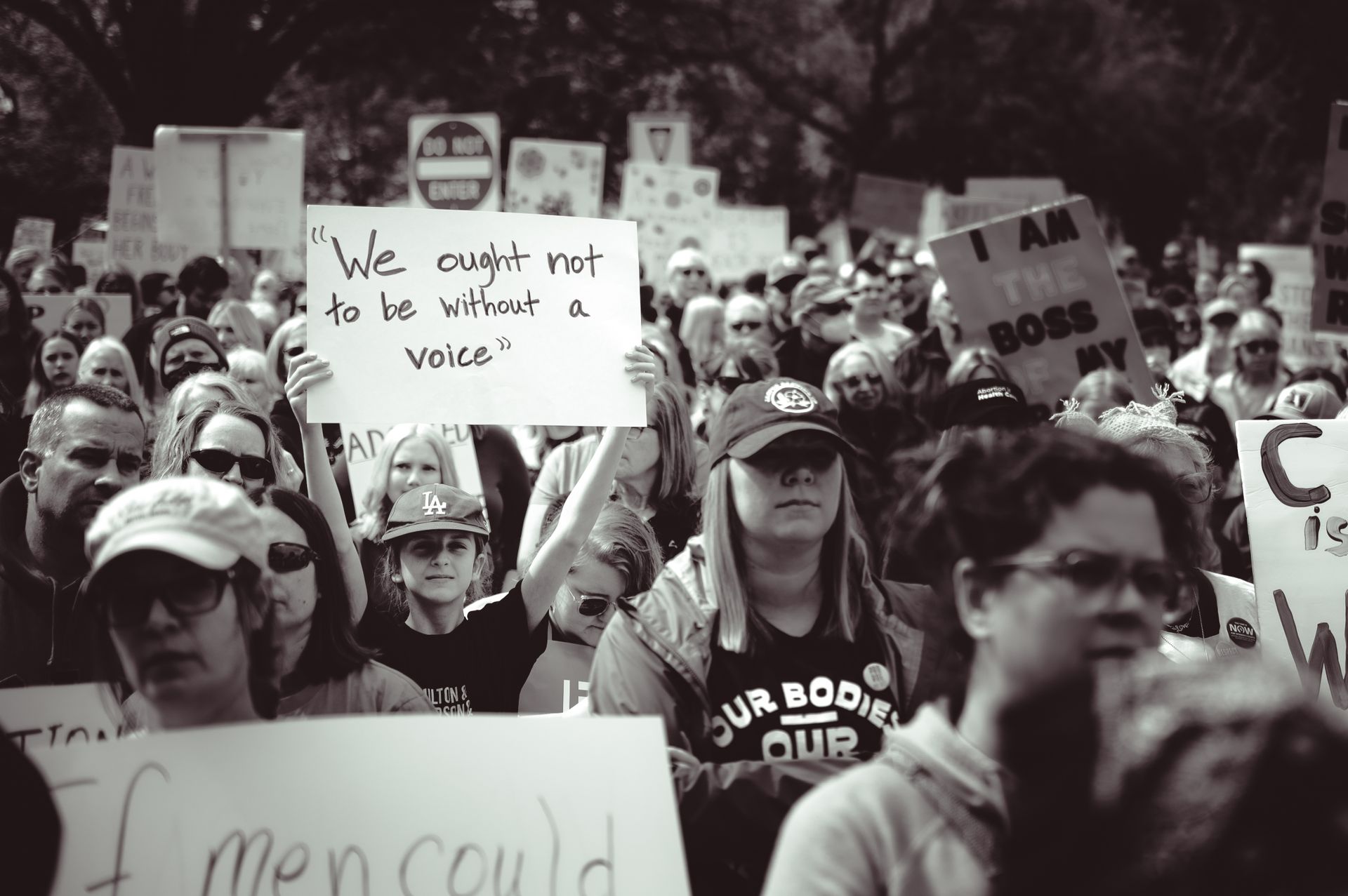 A large group of diverse people holding signs at an outdoor protest rally.