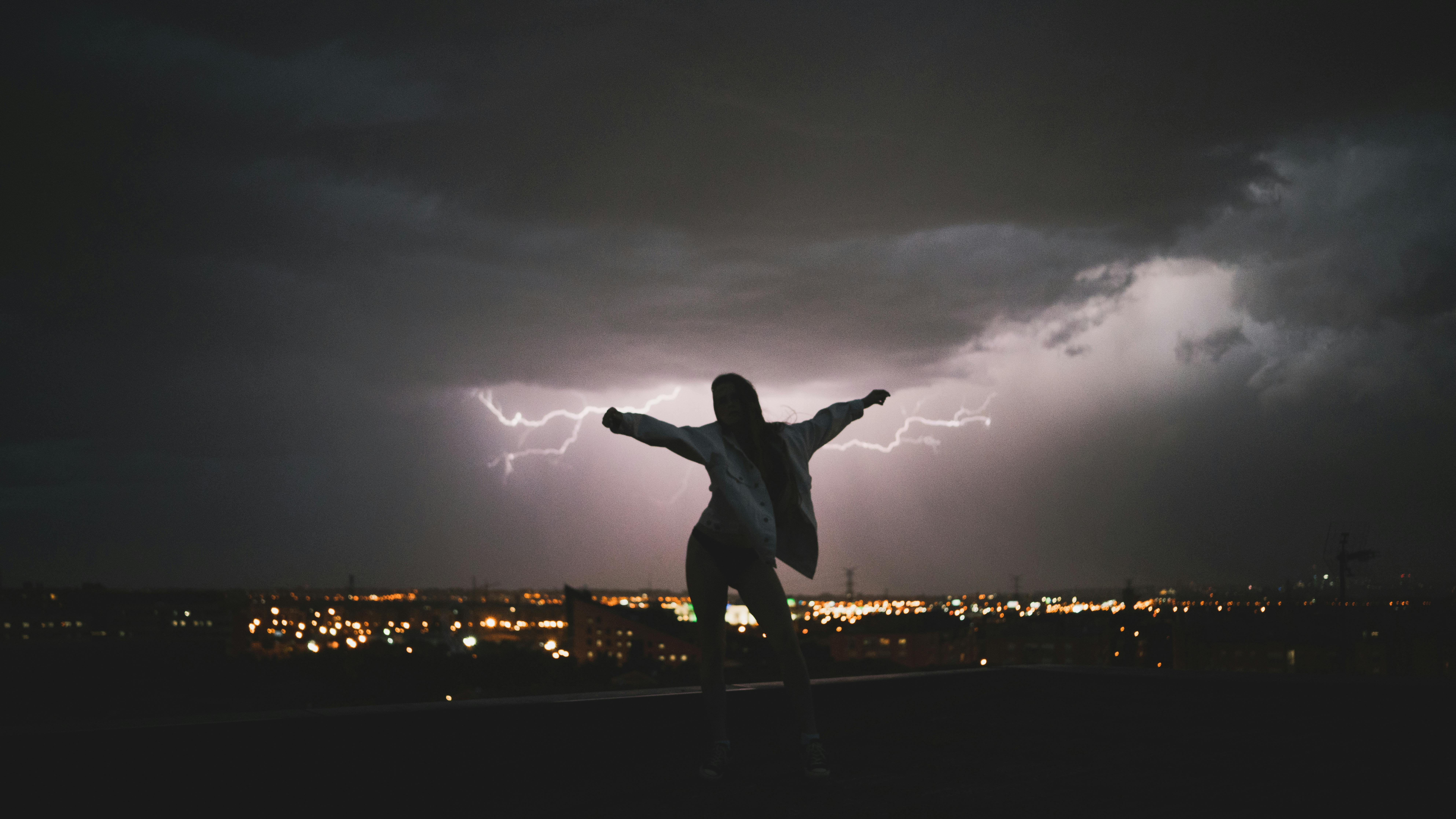 Silhouette of a woman with arms raised against a dramatic lightning storm at night.